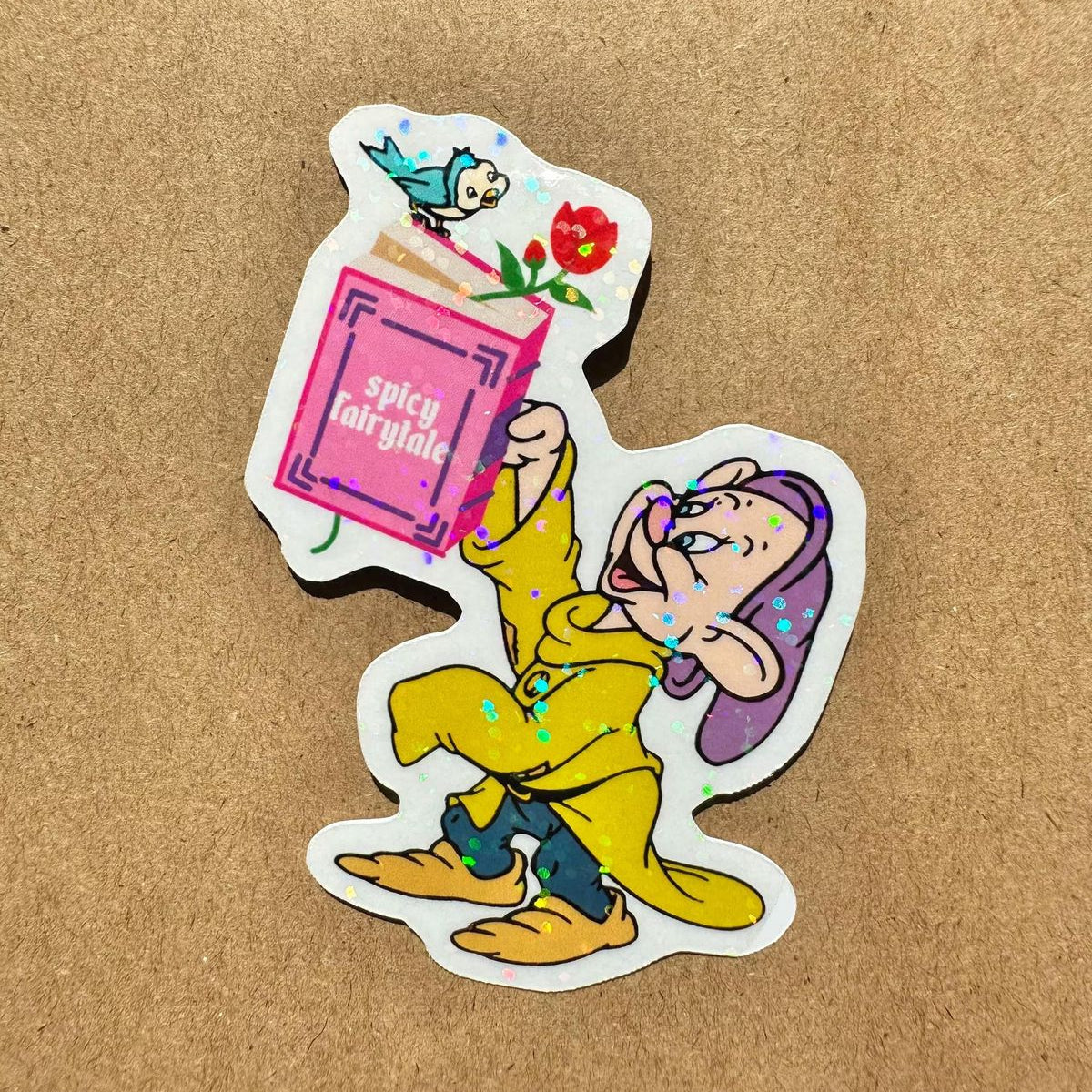 Sticker of a disney character, dopey,  in yellow coat holding a pink box labeled 'spicy fairy tale' on a brown background