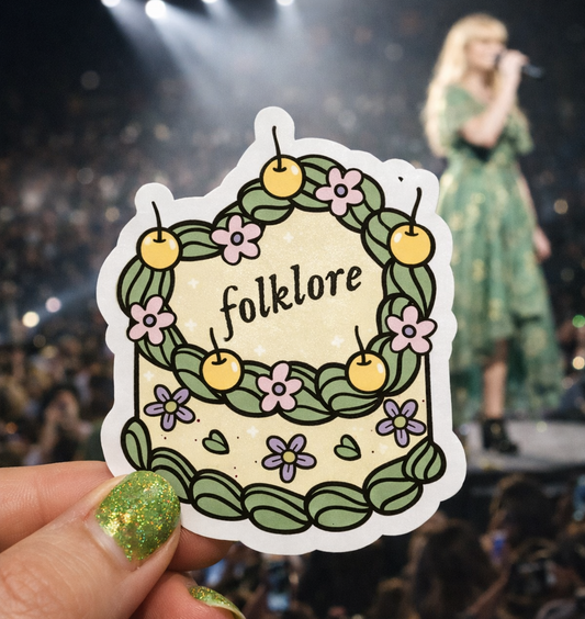 Sticker with 'folklore' design held by a hand in front of a concert crowd.
