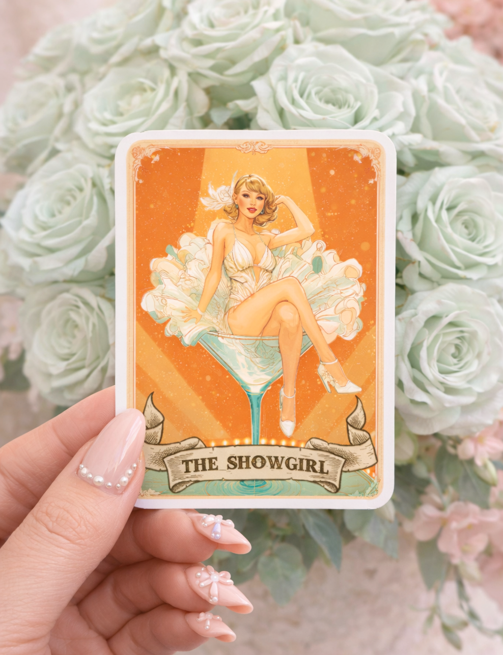 Card featuring 'The Showgirl' design held in front of green roses
