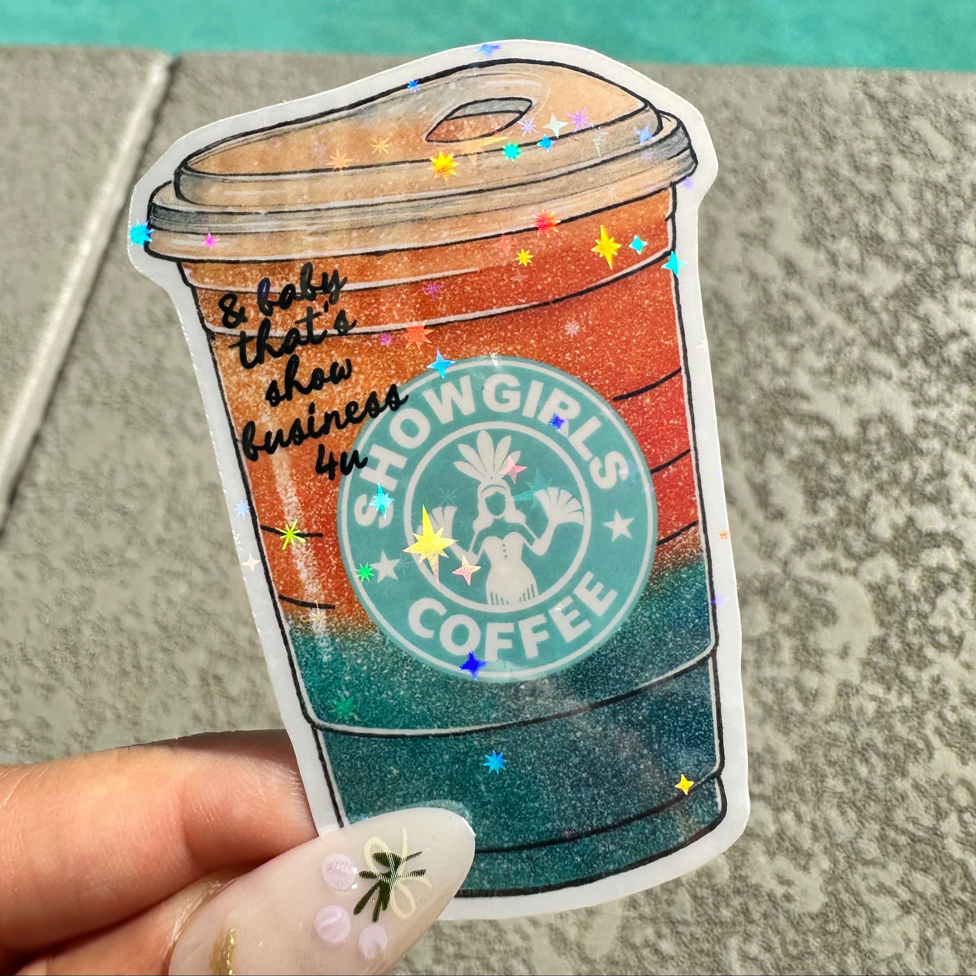 Sticker of a coffee cup with 'Showgirls Coffee' branding held by a hand.